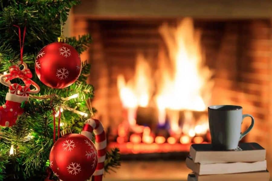 A christmas tree and a roaring fire with a pile of books and a coffee on top.