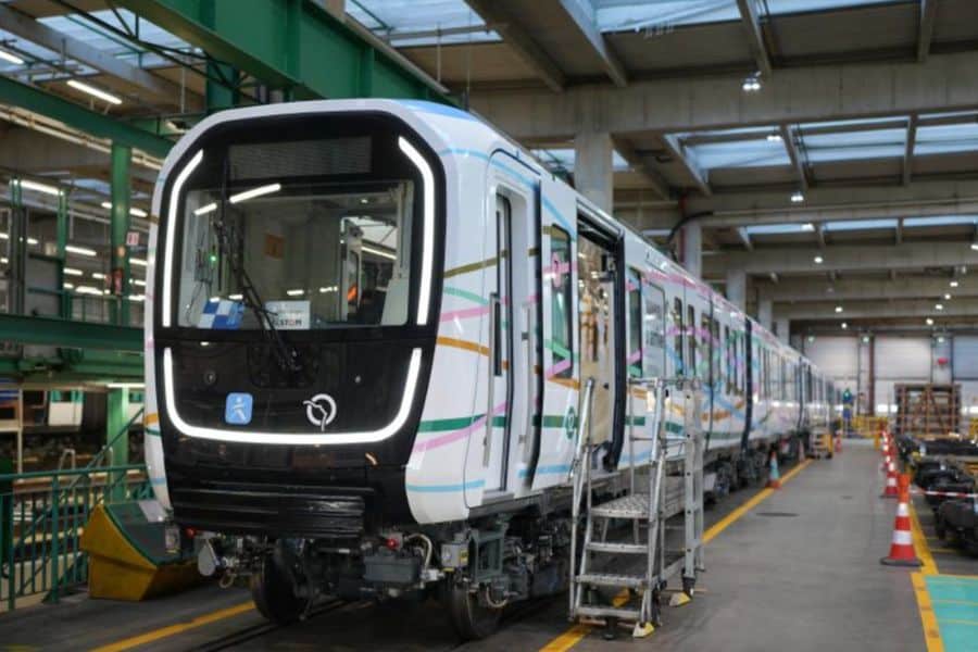 Front view of a modern Paris Metro train inside a large maintenance depot, with its headlights on and access stairs positioned at the open door. The train features a sleek black and white front accented by curved LED lights.