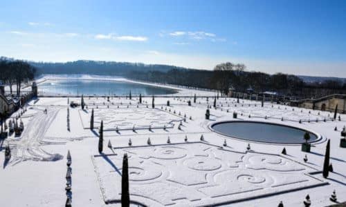The Orangery at the Palace of Versailles covered in snow under a blue sky.
