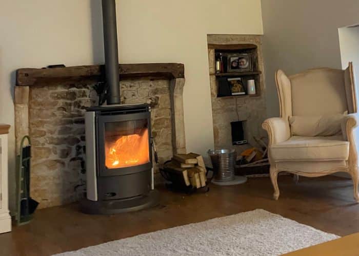 A roaring fire in a woodburning fire in a lounge in France with a cream rug in front of it.
