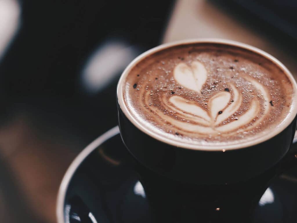 A small hot chocolate in a blue cup with a saucer and a flower on top done in frothy milk