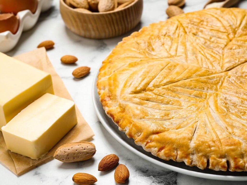 A pastry pie on a plate with two slabs of butter, some nuts and egges in a bowl on the side