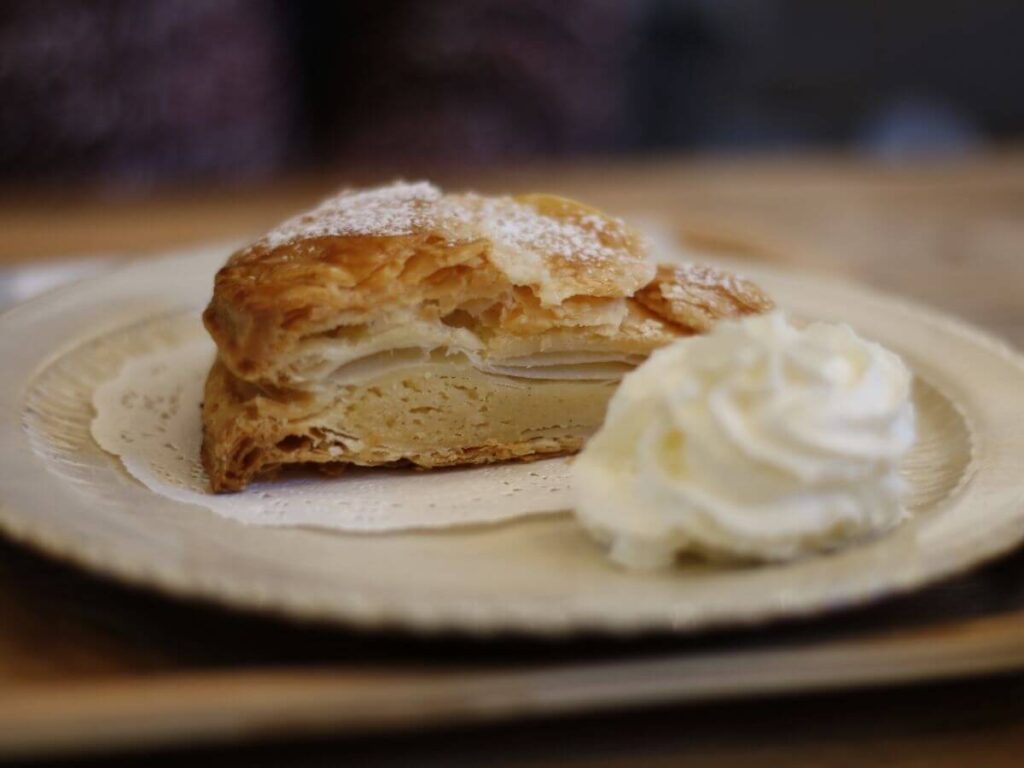A slice of pie on a plate with a big dollop of cream on the side