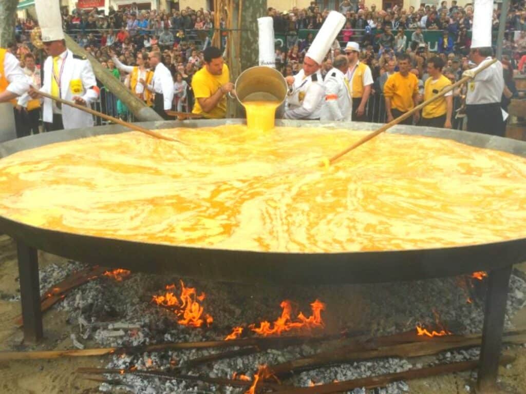 A giant omlette being cooked by a few chefs over a big fire in a street