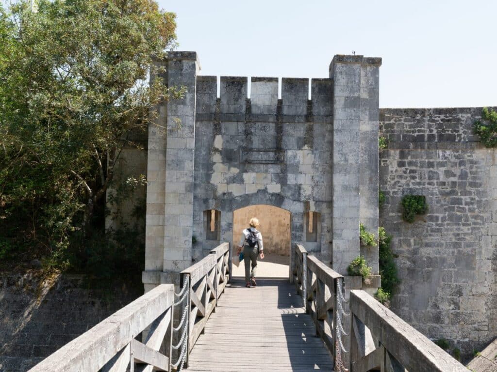 A man walking over a wooden bridge towards a stone tower