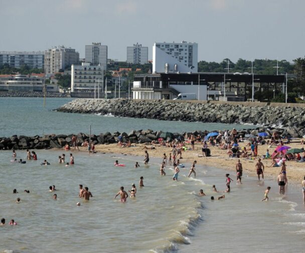 A beach with people swimming in the sea and lying on the sand