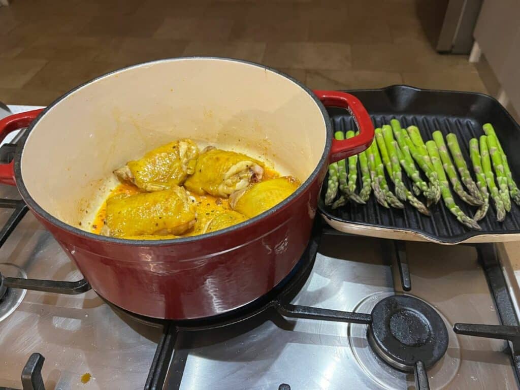 Chicken thighs in a pot and ggreen asparagus in a pan