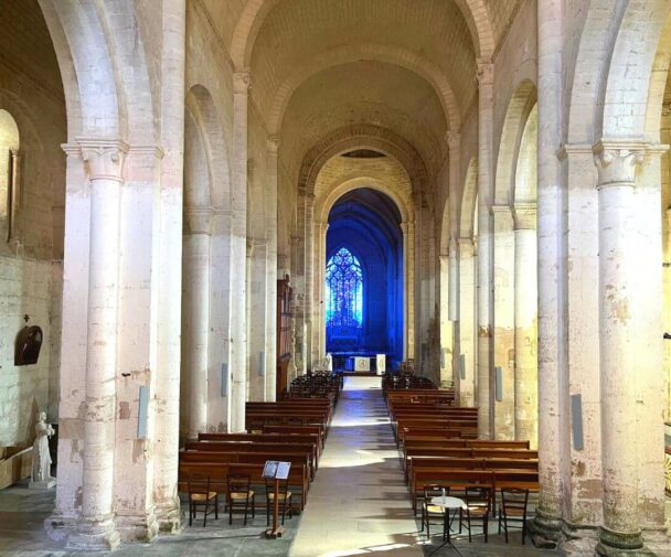 Inside of a church of abbey in France with a blue stained glass window