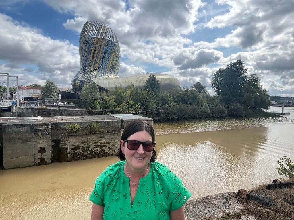 A lady sat in front of the cite du vin in Bordeaux with a river in front and a cloudy sky