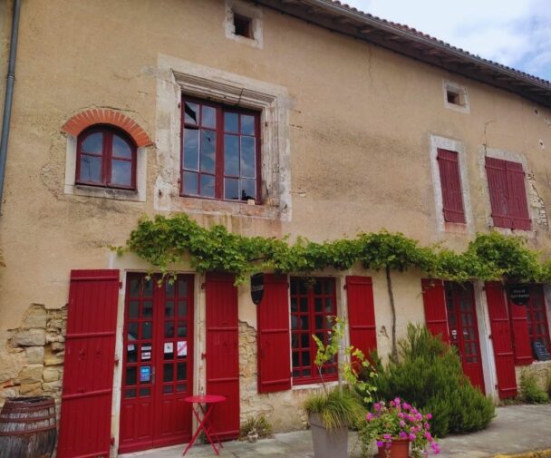 An old stone building with red shutters and doors in a rural French village