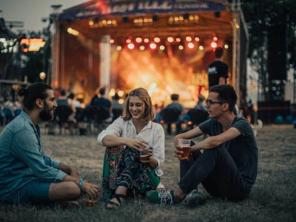 Three people sat on the grass at a music festival