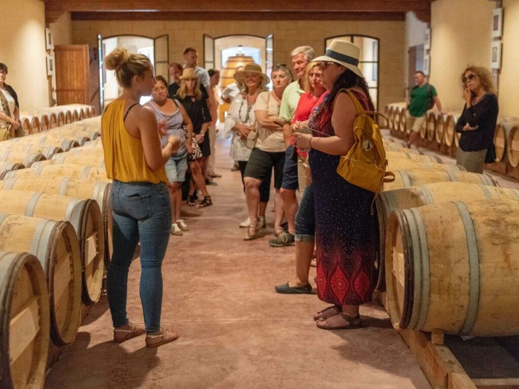 A group of people on a wine tasting tour in Bordeaux next to some barrels