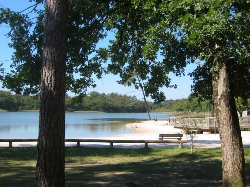 A lake with a sandy beach surrounded by trees in Aubeterre-sur-Dronne