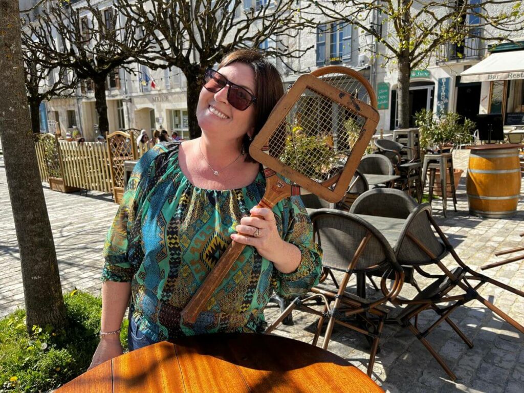 A woman holding a tennis racket in the market square in Aubeterre-sur-Dronne