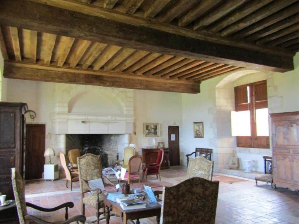 An old tiled sitting room with chairs and a big fireplace in the Chateau de Bayers