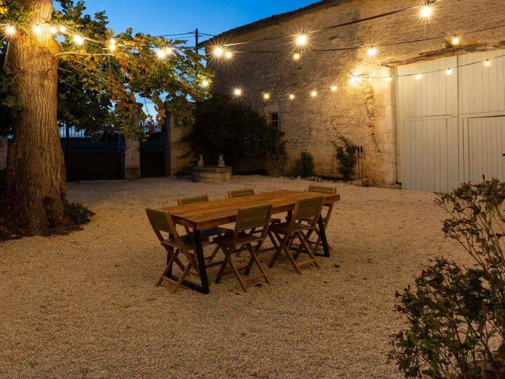 A pebbled courtyard at night with fairylights and a picnic bench in the Charente in France