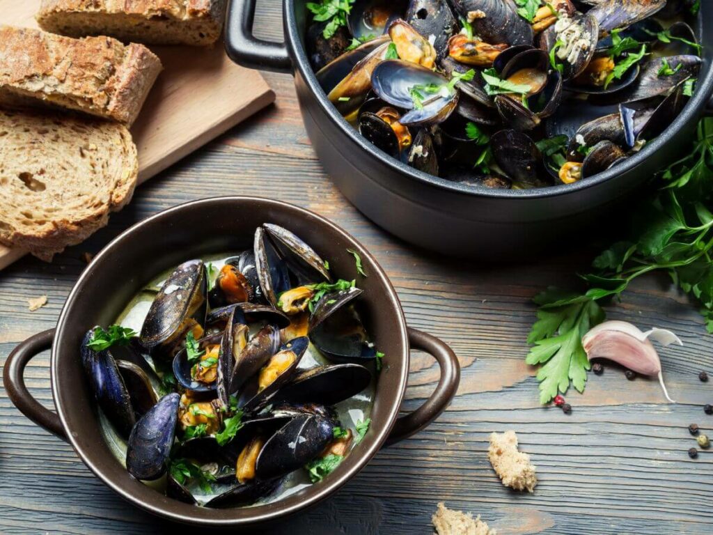 Two tins filled with cooked mussels in white wine sauce