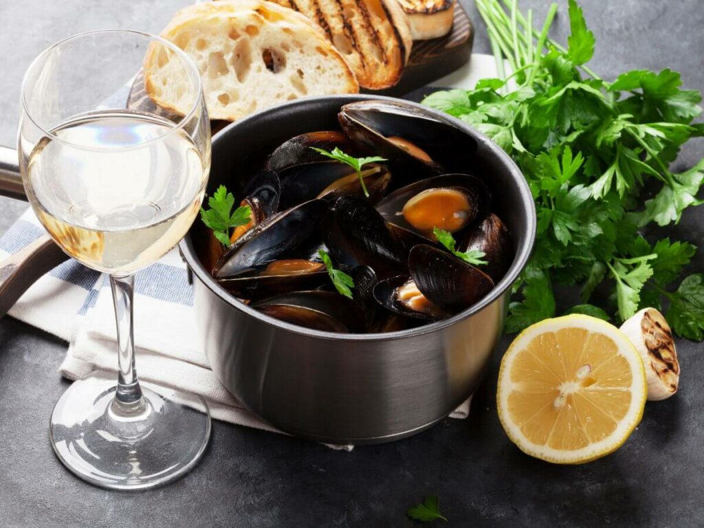 A pot of mussels in a creamy white wine sauce with a glass of wine and French bread