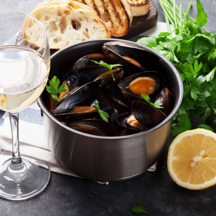 A pot of mussels in white wine sauce with a glass of wine and French bread