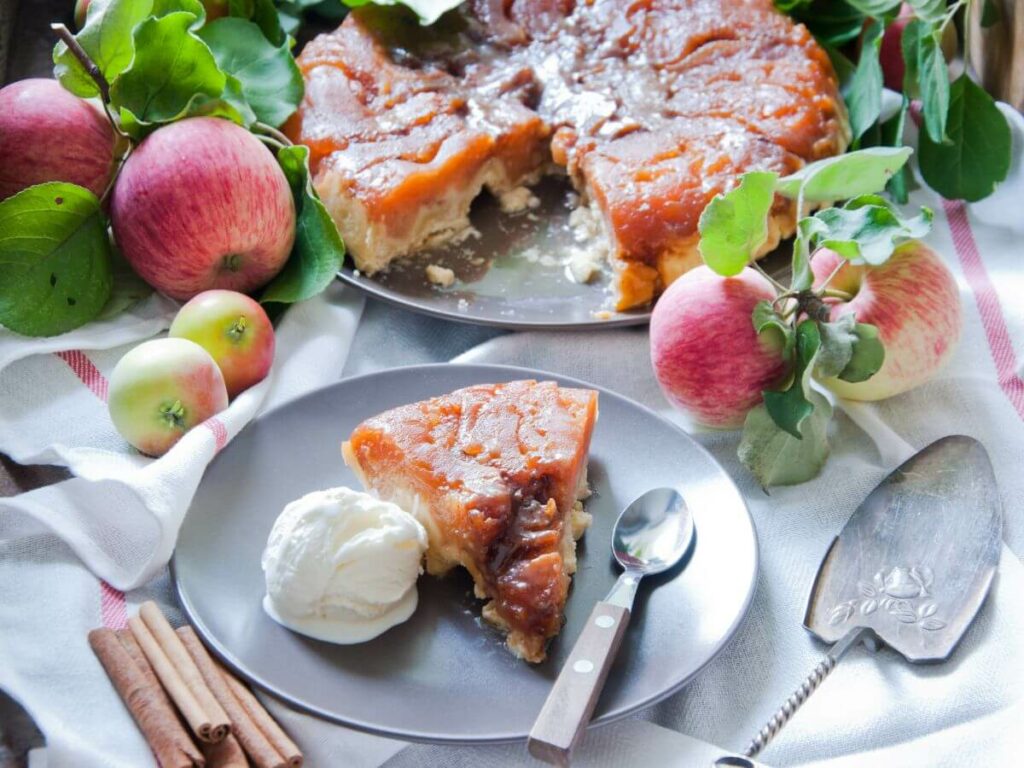 A slice of tarte tatin wiht icecream surrounded by apples and more apple pie
