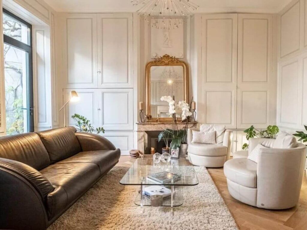 A beautifully designed lounge with a brown sofa, big gold gilded mirror and wooden floors with a cream rug