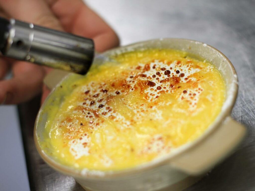 Someone holding a kitchen blow torch on a creme brulee to caramelise the sugar