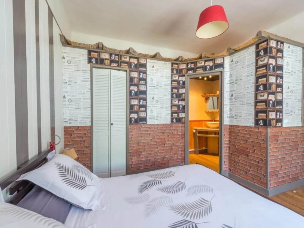 A bedroom with a double bed and white duvet and wallpapered walls with seaside decoration