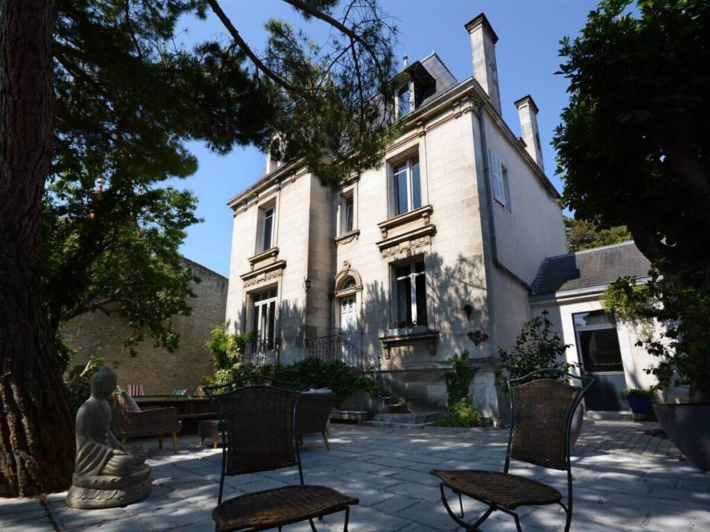 The outside of a rendered house in La Rochelle with a garden and two chairs with trees