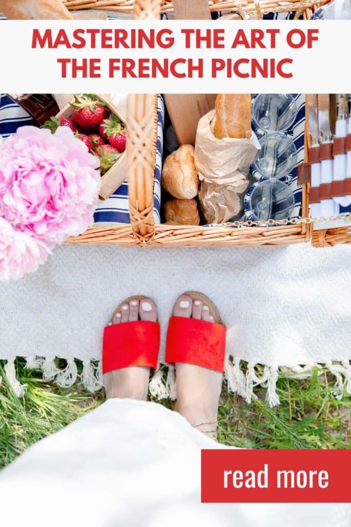 A top-down view of a French picnic basket, elegantly packed with baguettes, strawberries, wine glasses, and a bouquet of pink peonies. A person wearing red sandals stands on a picnic blanket, capturing the essence of a stylish outdoor meal.