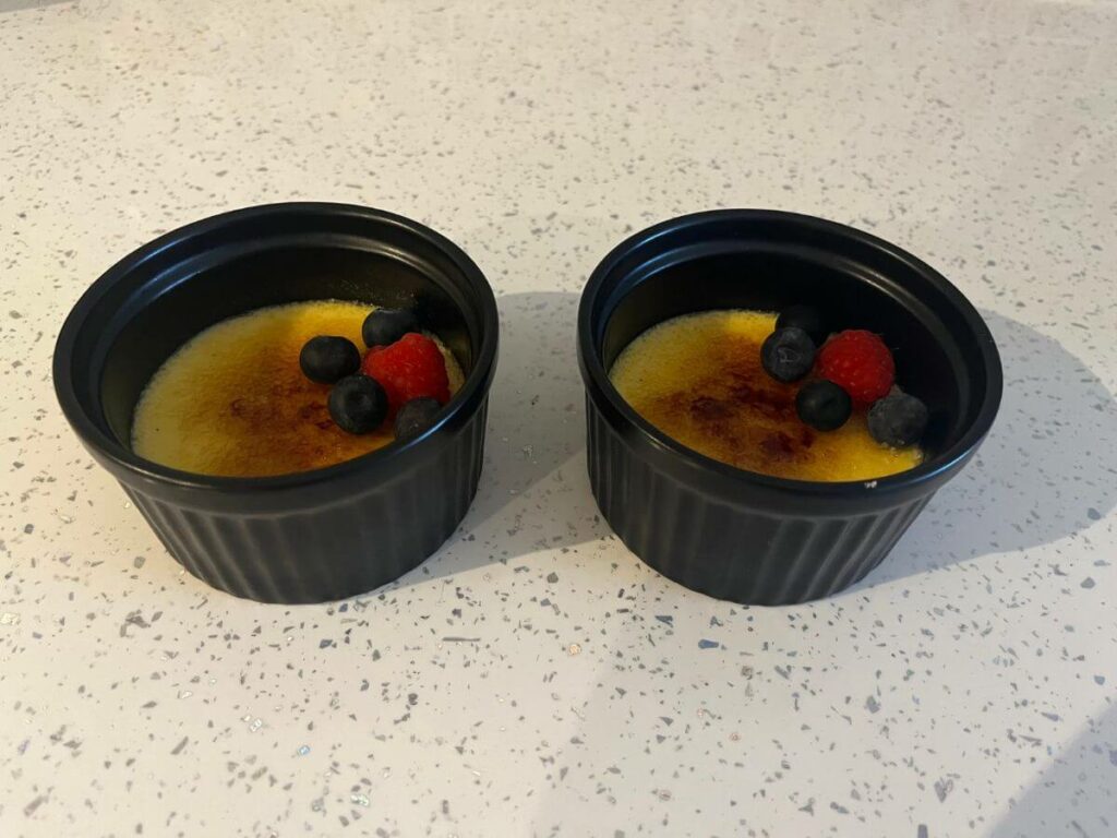 Two ramekins with creme brulee topped with blueberries