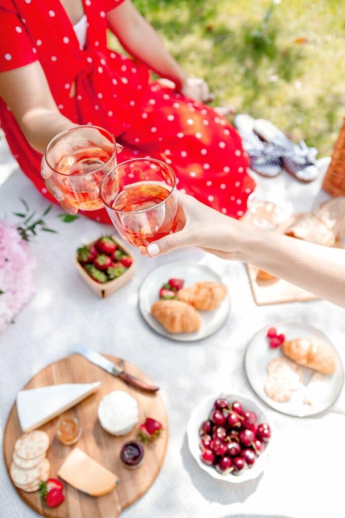 A deliciously styled picnic featuring croissants, fresh fruit, artisanal cheeses, and crispy baguettes. Elegant tableware and a floral bouquet complete the picturesque French countryside meal.