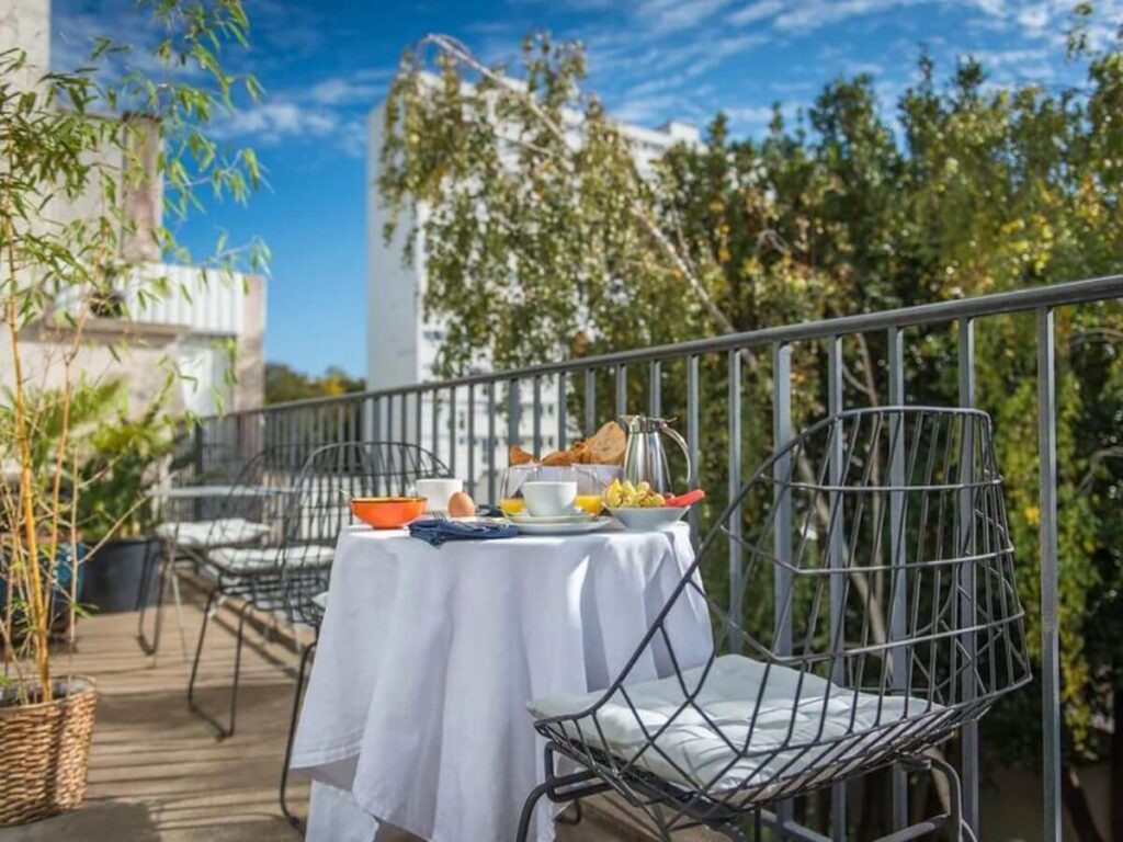 A terrace balcony set up for breakfast with a table and a white table cloth and two chairs