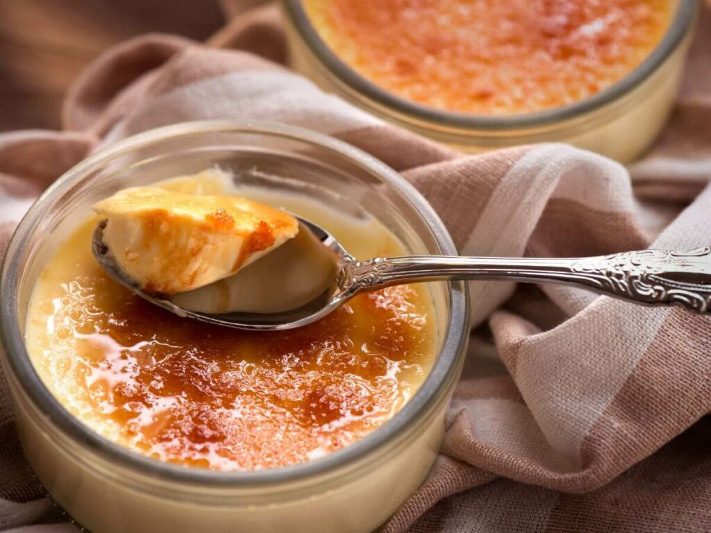 A ramekin with creme brulee with a spoon sat on brown material