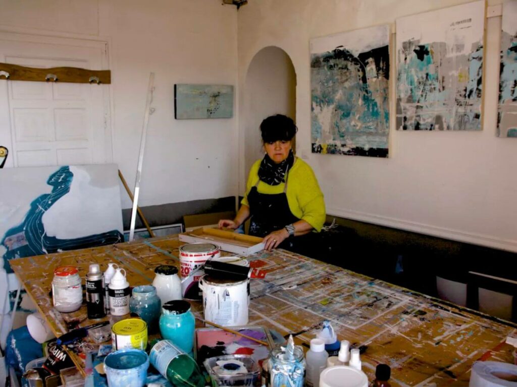 An artist in her studio in France surrounded by paint pots and canvases