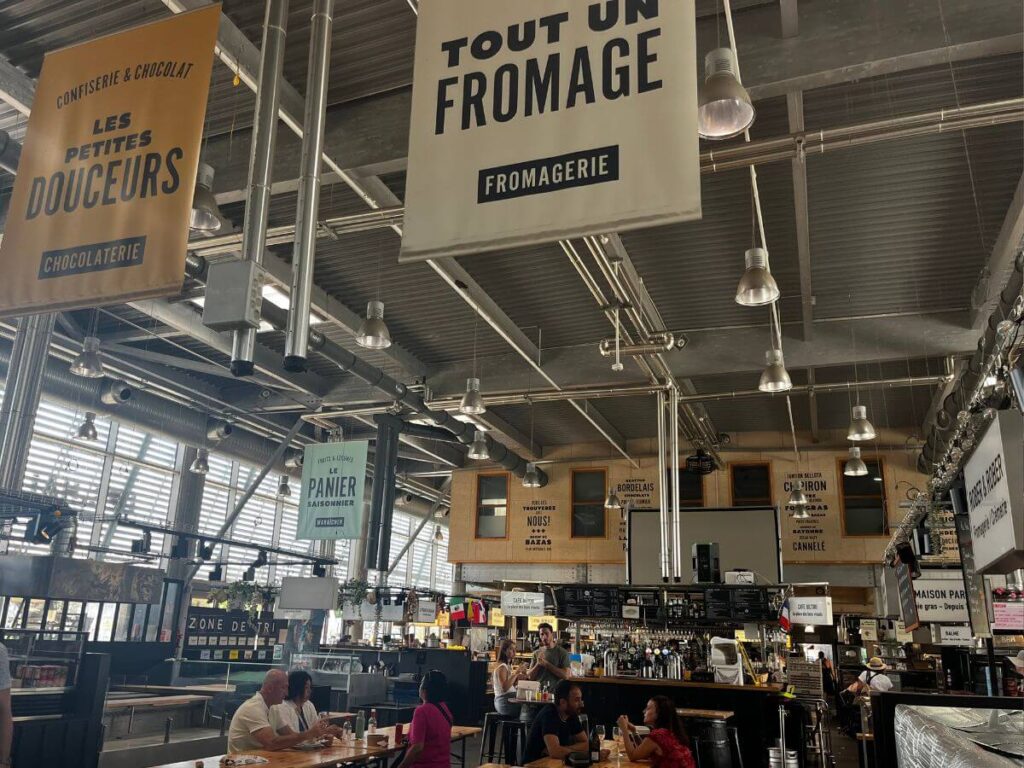 A market hall in Bordeaux with a cheese sign and lots of stalls inside.