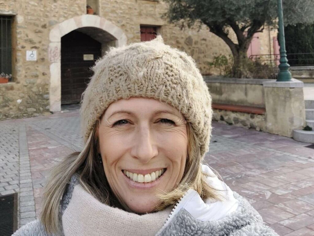 A lady in a woollu hat stood in front of a stone building