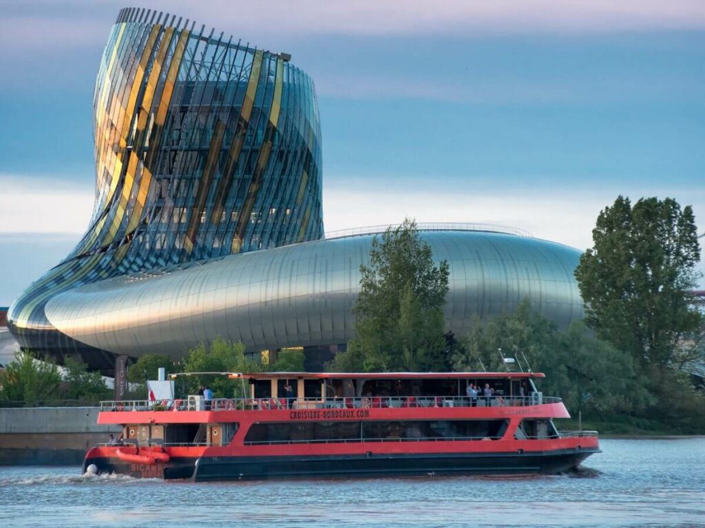 A red boat on the river Garonne with the cite du vin in the background