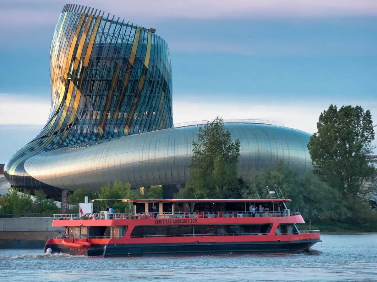 A red boat on the river Garonne with the cite du vin in the background