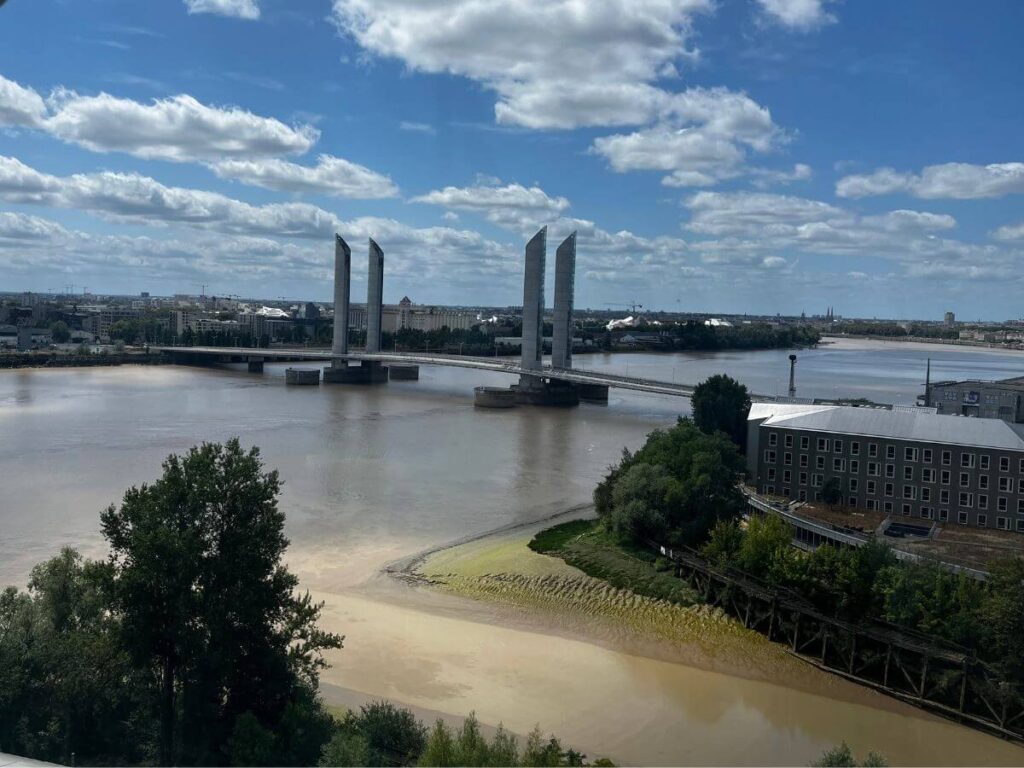 A birds eye view of Bordeaux and the river Gironde with a bridge going over it against a blue sky