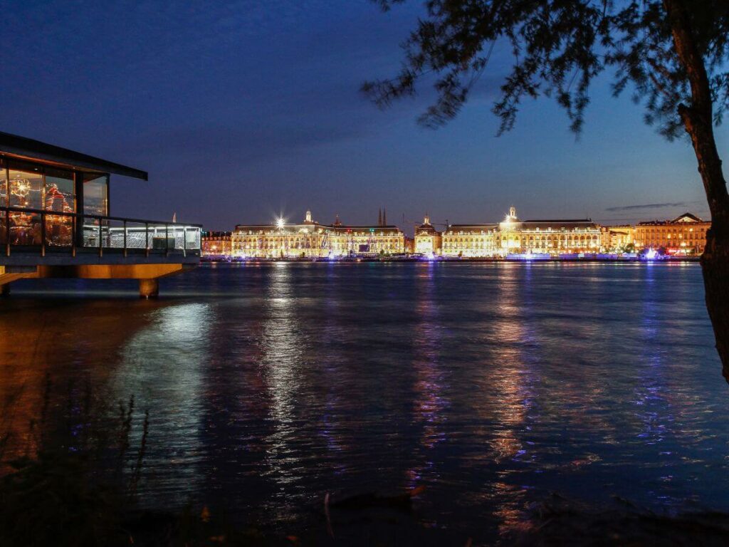 A night time view of a river in Bordeaux with a cityscape in the distance
