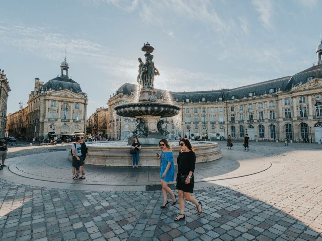 A square in Bordeaux with a fountain in the middle and people walking around
