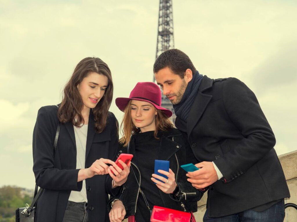 Two women and a man stood in front of the Eiffel Tower in Paris looking at a phone to see if there is Amazon in France