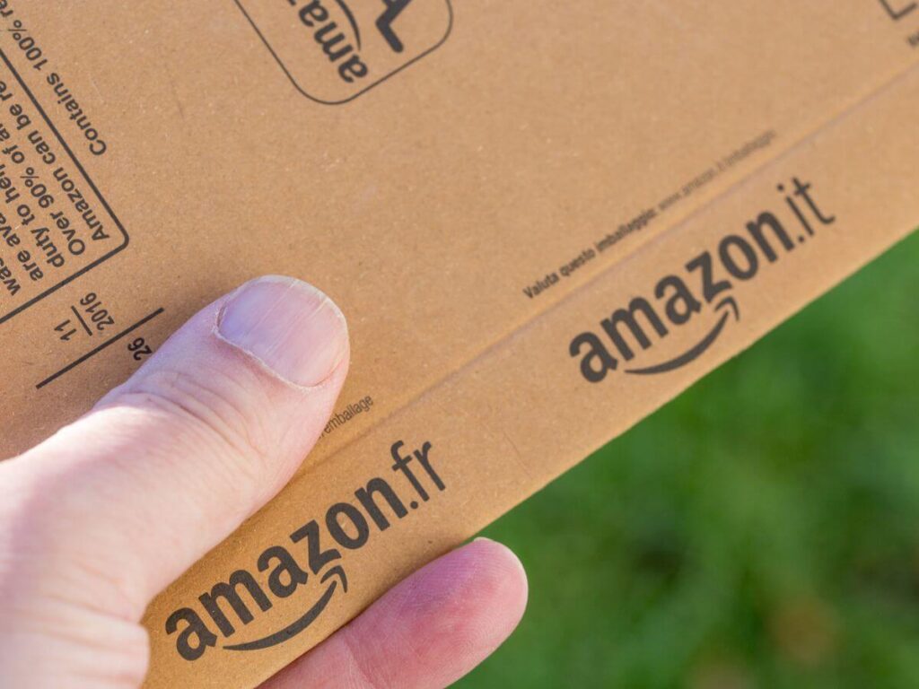 A hand holding a brown amazon.fr envelope with a green background