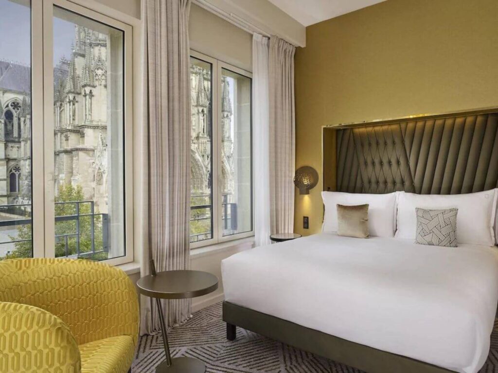 A hotel bedroom with mustard yellow wall and armchair and a cathedral in the background out the window