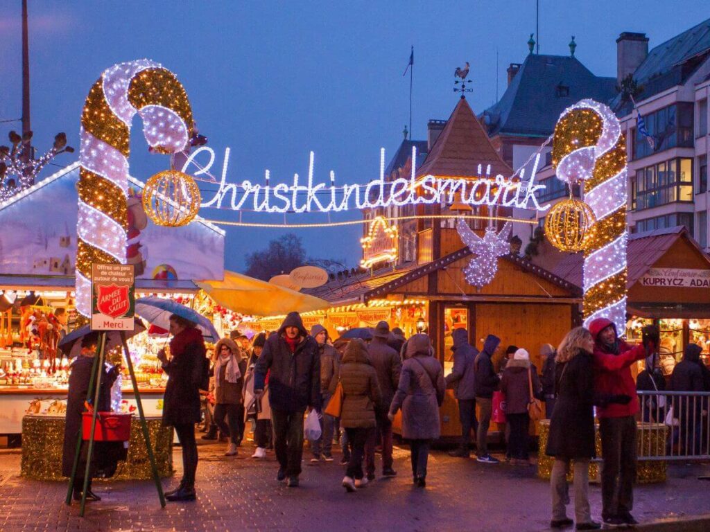 A sign with the Christkindelsmarik sign and two giant candy canes either side at night and people walking around