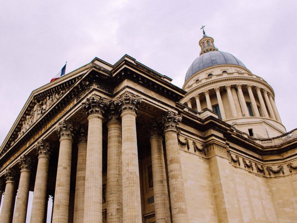 A large building with big stone columns and a rounded dome on top with a cross in paris