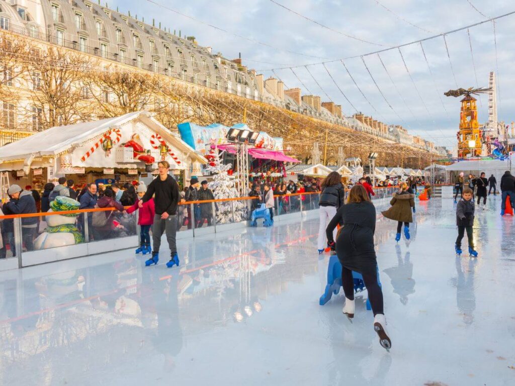 An ice rink in Paris at the Tuileries Christmas Market with people skating and chalets all around