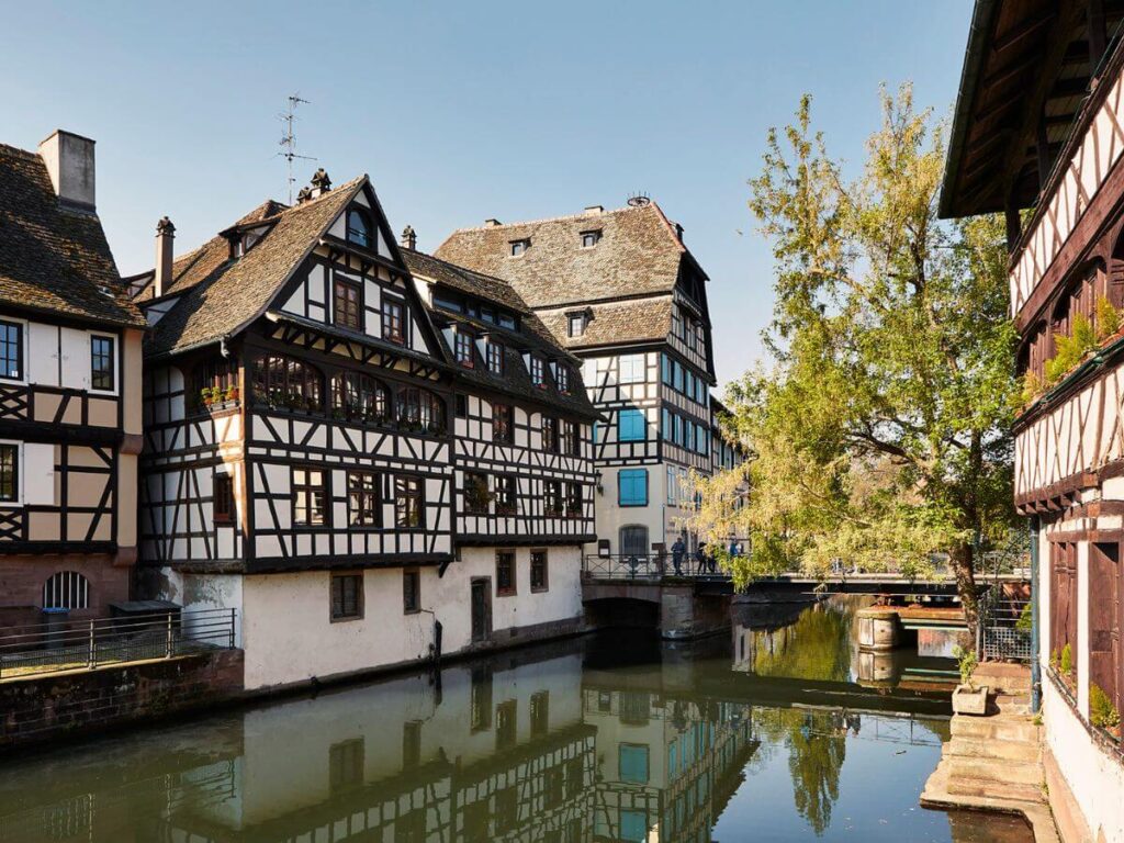 Half-timbered buildings in Strasbourg along a river bank with some trees in the background