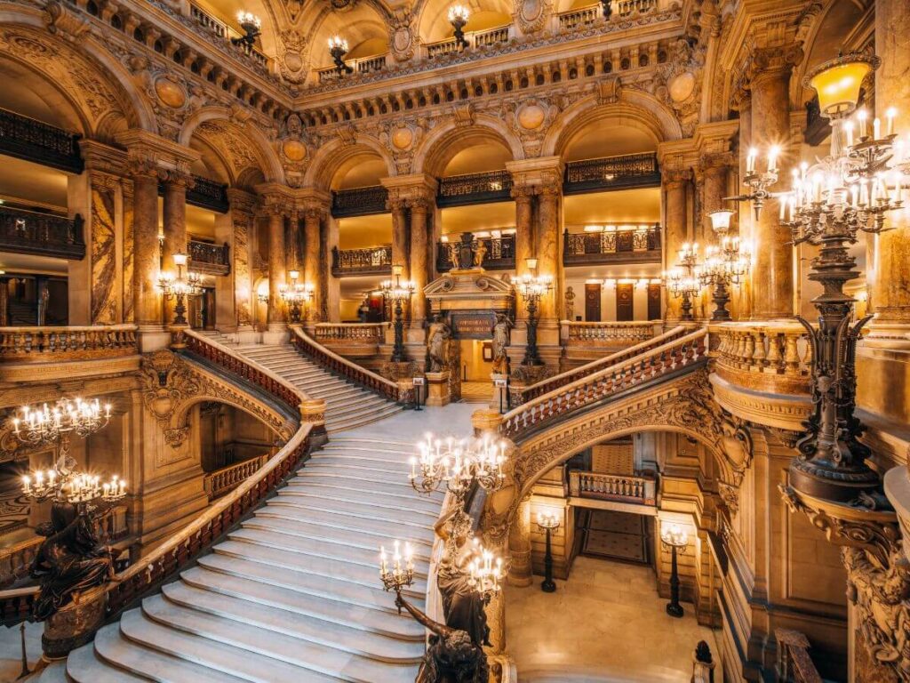 An opulent candlelit staircase with lots of ornate carvings in wood and gold