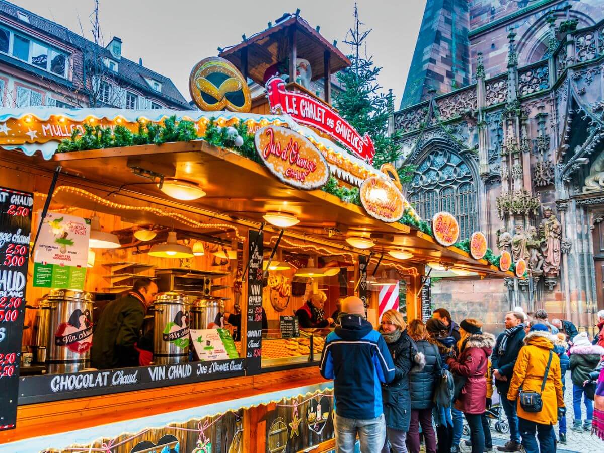 A vat of mulled wine and a bowl with an orange, aniseed and people in the background